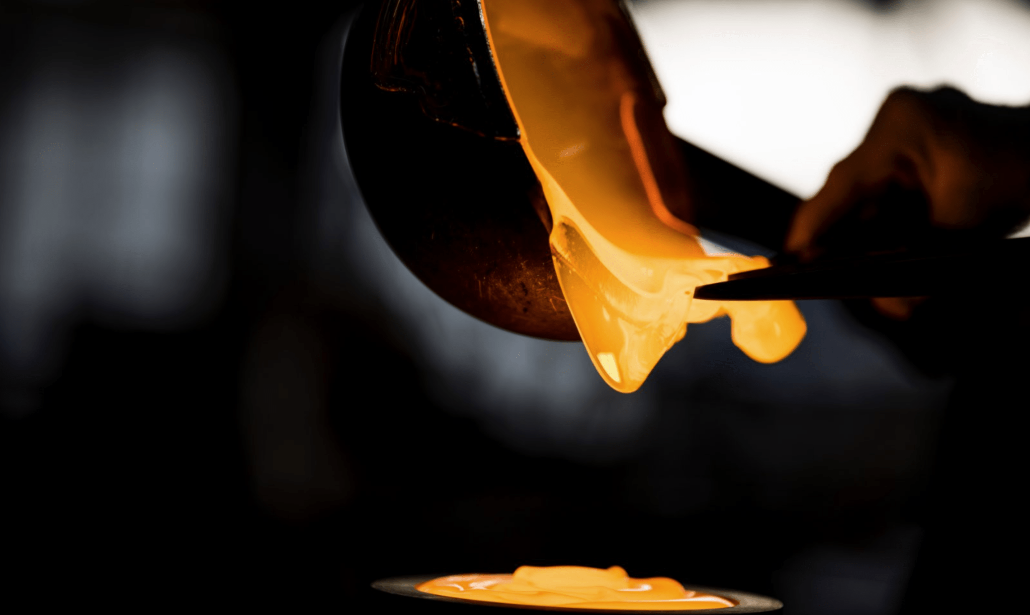 Glassblower shaping molten glass with a tool against a dark background