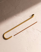 Brass hook incense holder with incense stick on textured surface