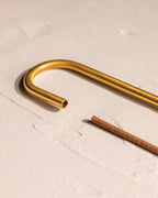 Close-up of curved brass-finished incense holder with incense stick