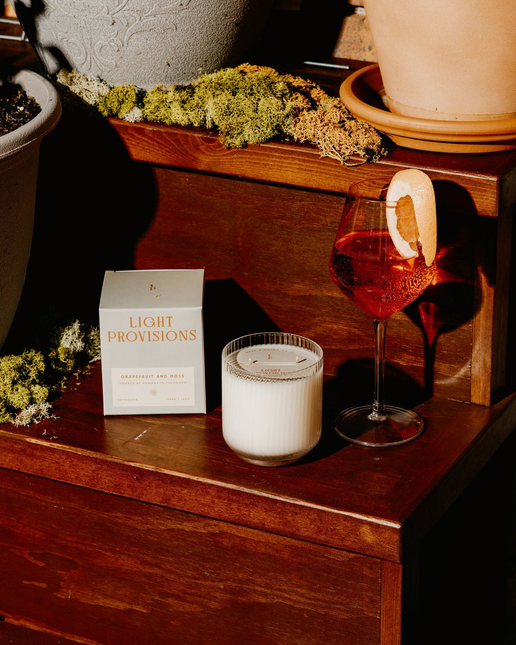 Candle, glass of red wine, and 'Light Provisions' box on a wooden surface.