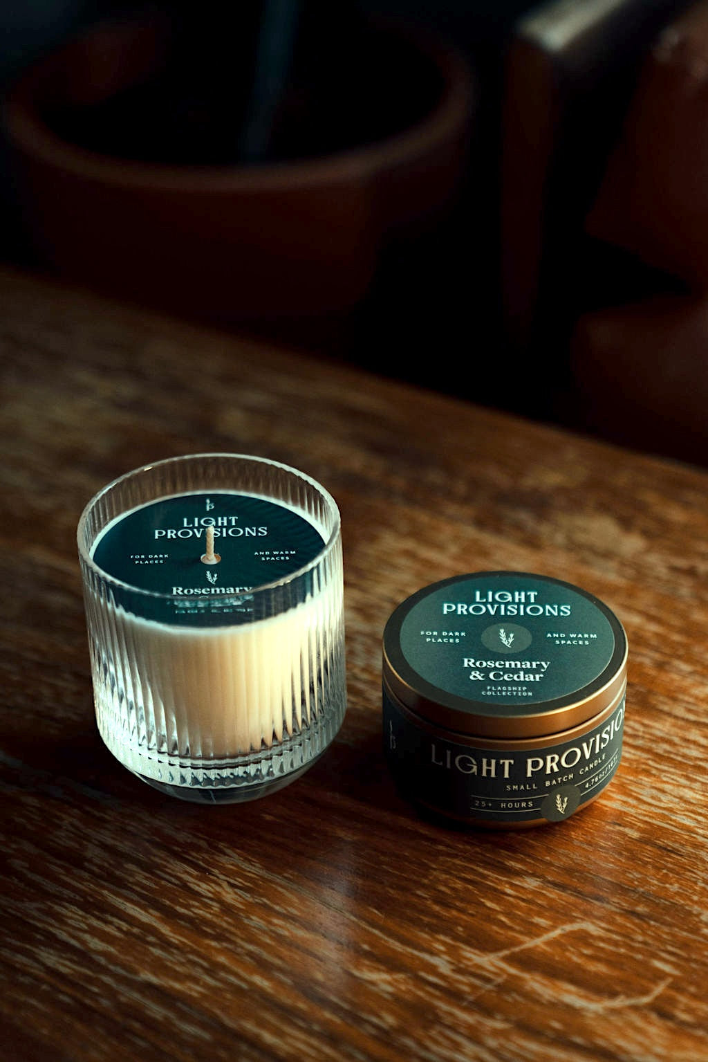 Tumbler and closed tin side by side on the table; lids show Rosemary & Cedar branding; dramatic side lighting for a cozy, at-home feel.