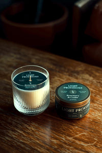 Tumbler and closed tin side by side on the table; lids show Rosemary & Cedar branding; dramatic side lighting for a cozy, at-home feel.