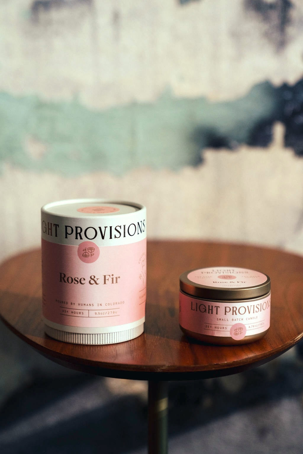Rose & Fir candle and matching tube packaging on a wooden table with textured wall backdrop