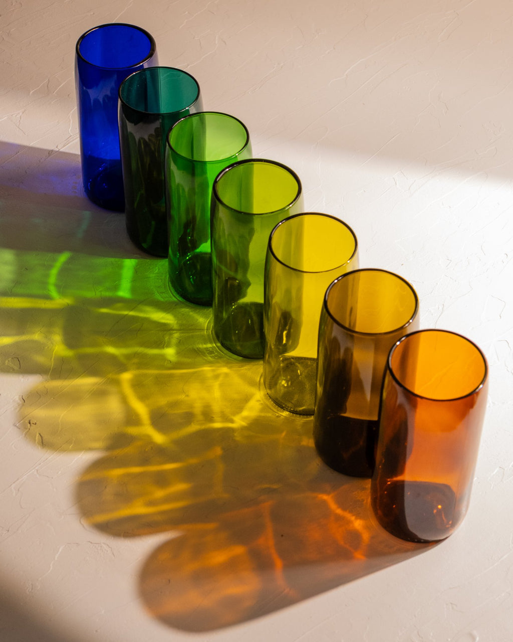 Recycled wine bottle incense vases in cobalt, teal, emerald, champagne green, olive, antique green, and amber glass casting colorful shadows.
