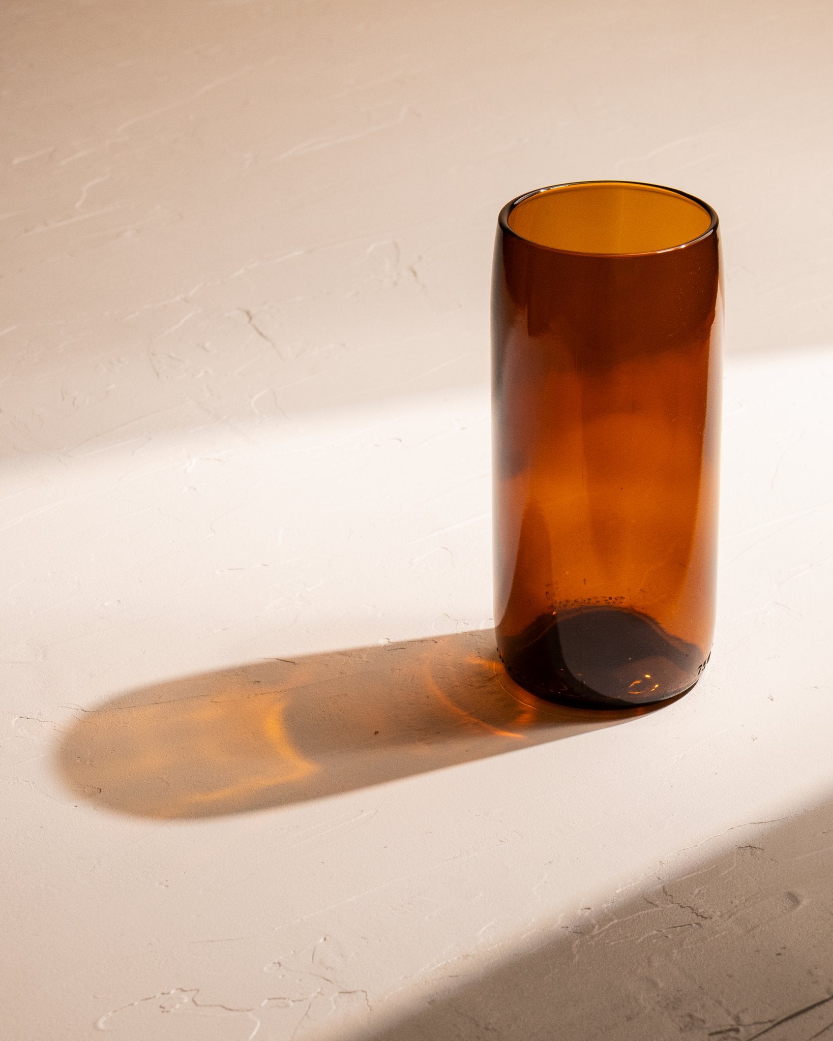 Amber recycled wine bottle incense vase casting a warm amber shadow.