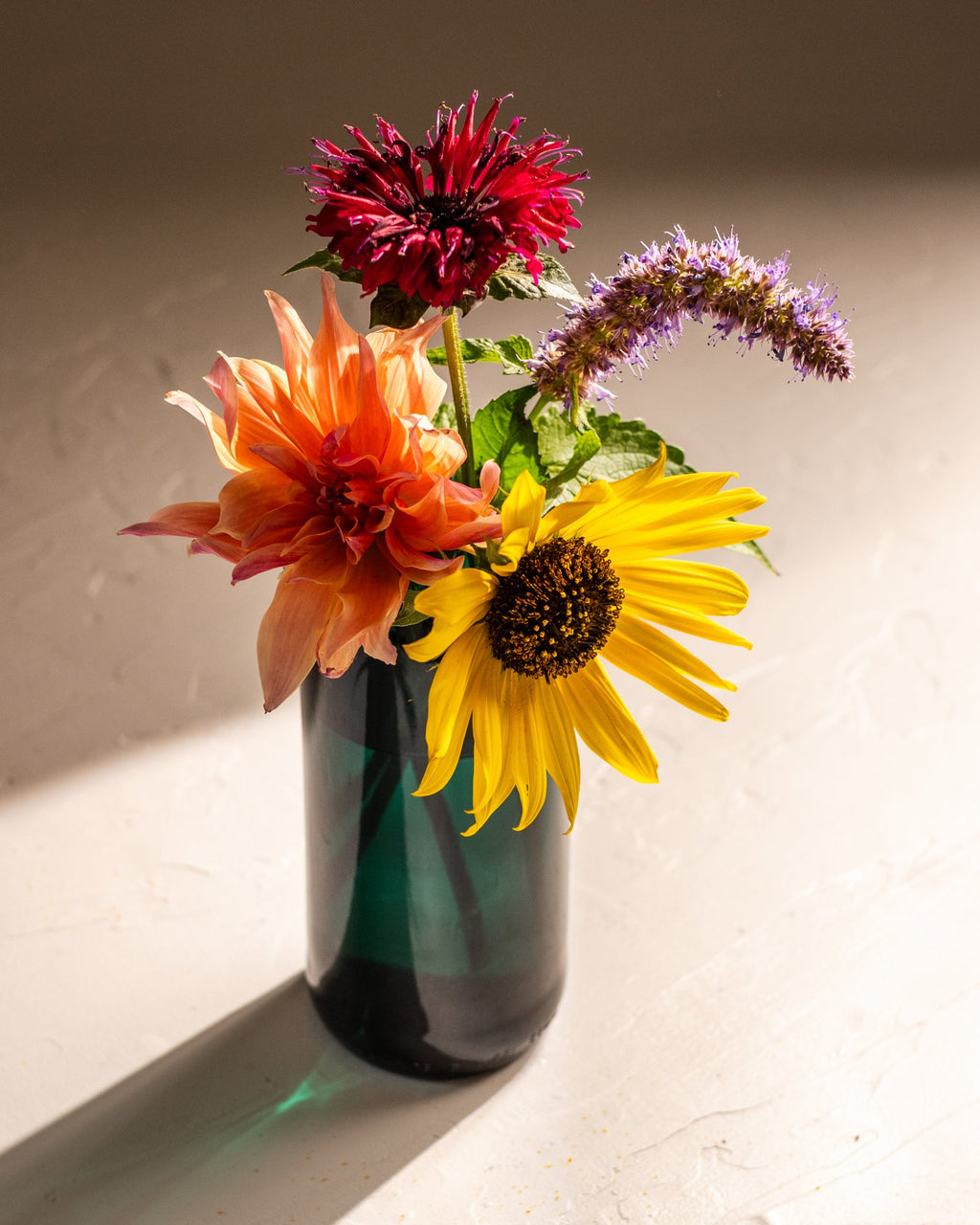 Recycled teal wine bottle vase filled with colorful fresh flowers in warm sunlight.
