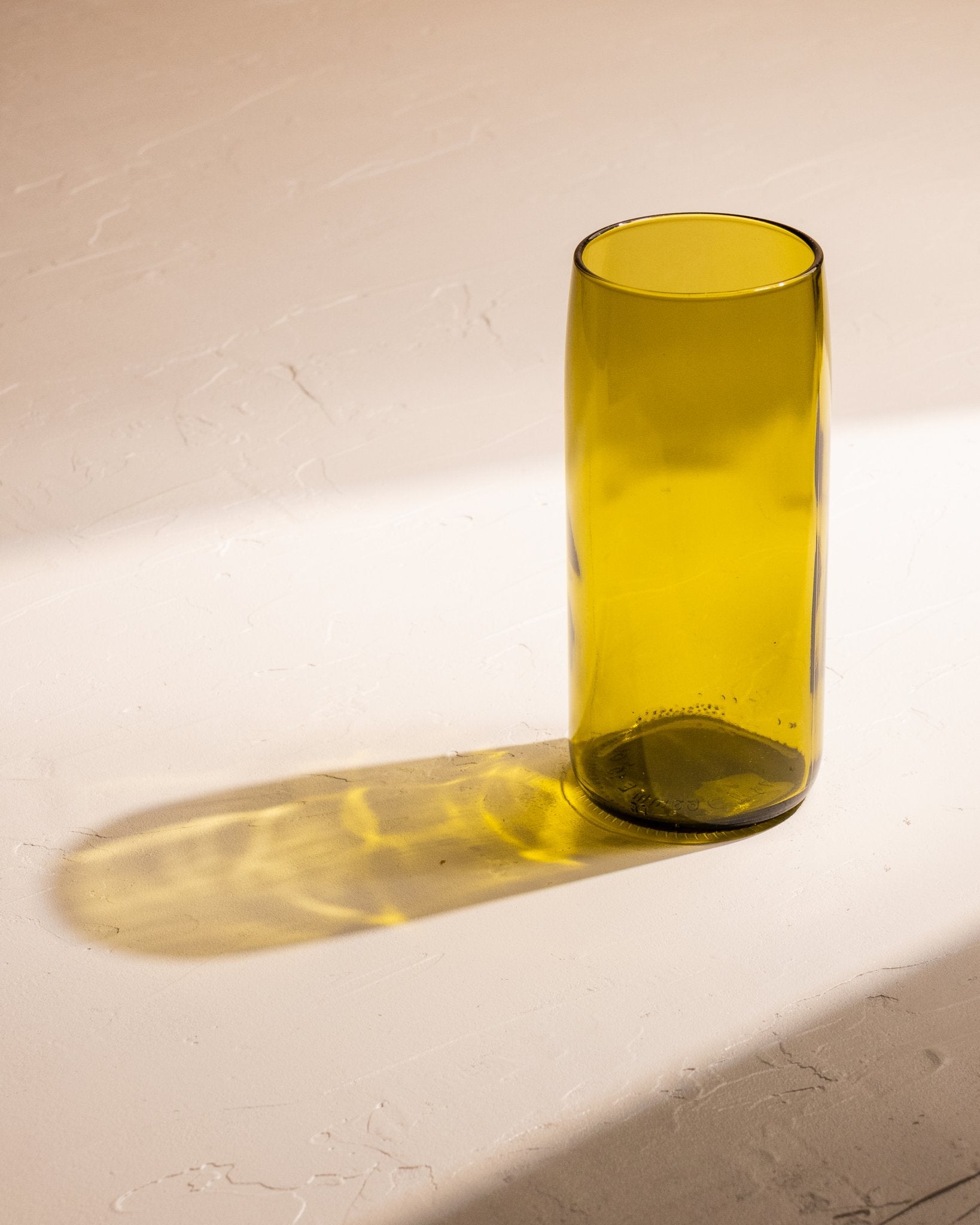 Olive recycled wine bottle incense vase casting a bright golden shadow.