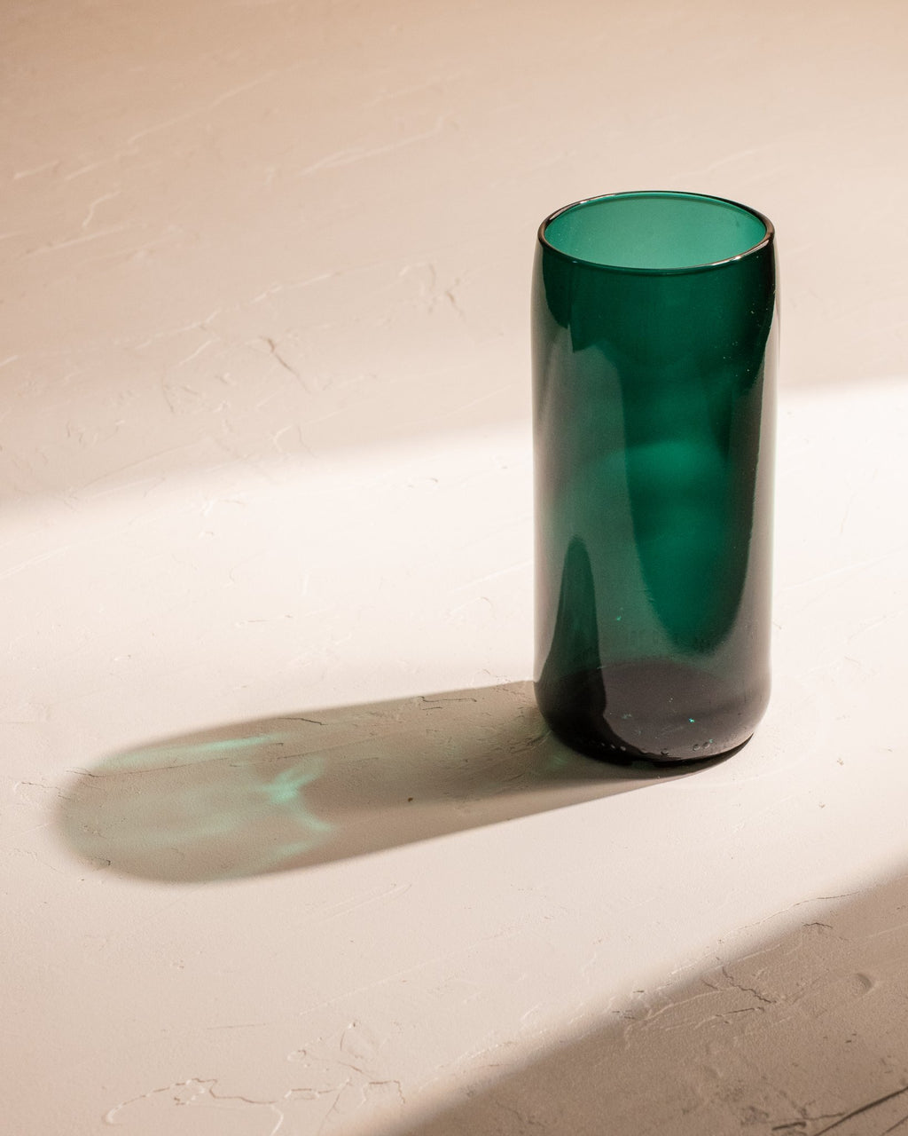 Teal recycled wine bottle incense vase casting a long green-blue shadow in sunlight.