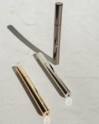 Tsubota Pearl Sigaretta stick lighters in gold, silver, and black, with one standing upright and two lying on a pale surface.
