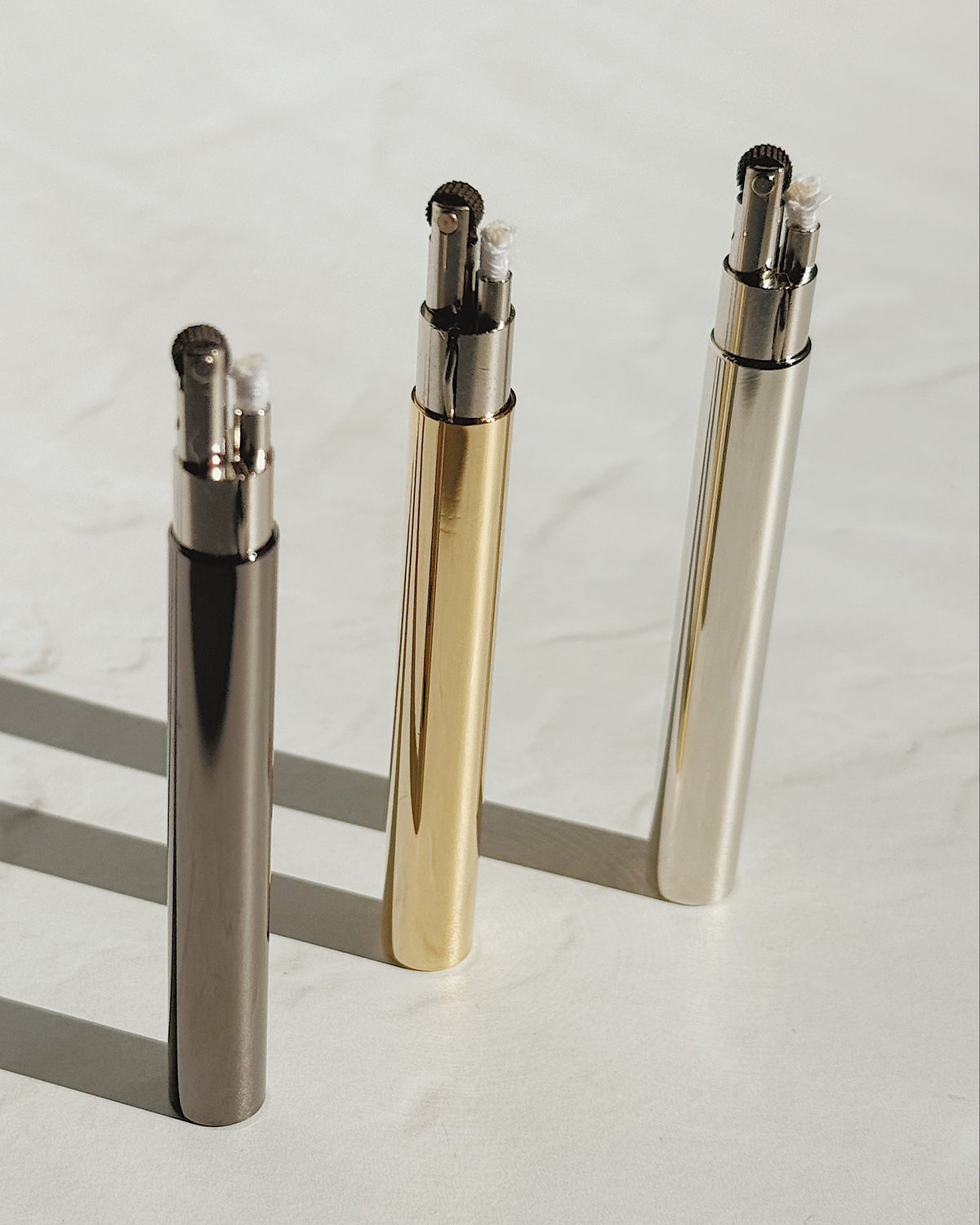 Three Tsubota Pearl Sigaretta stick lighters standing upright with caps removed, showing the wicks and flint wheels.