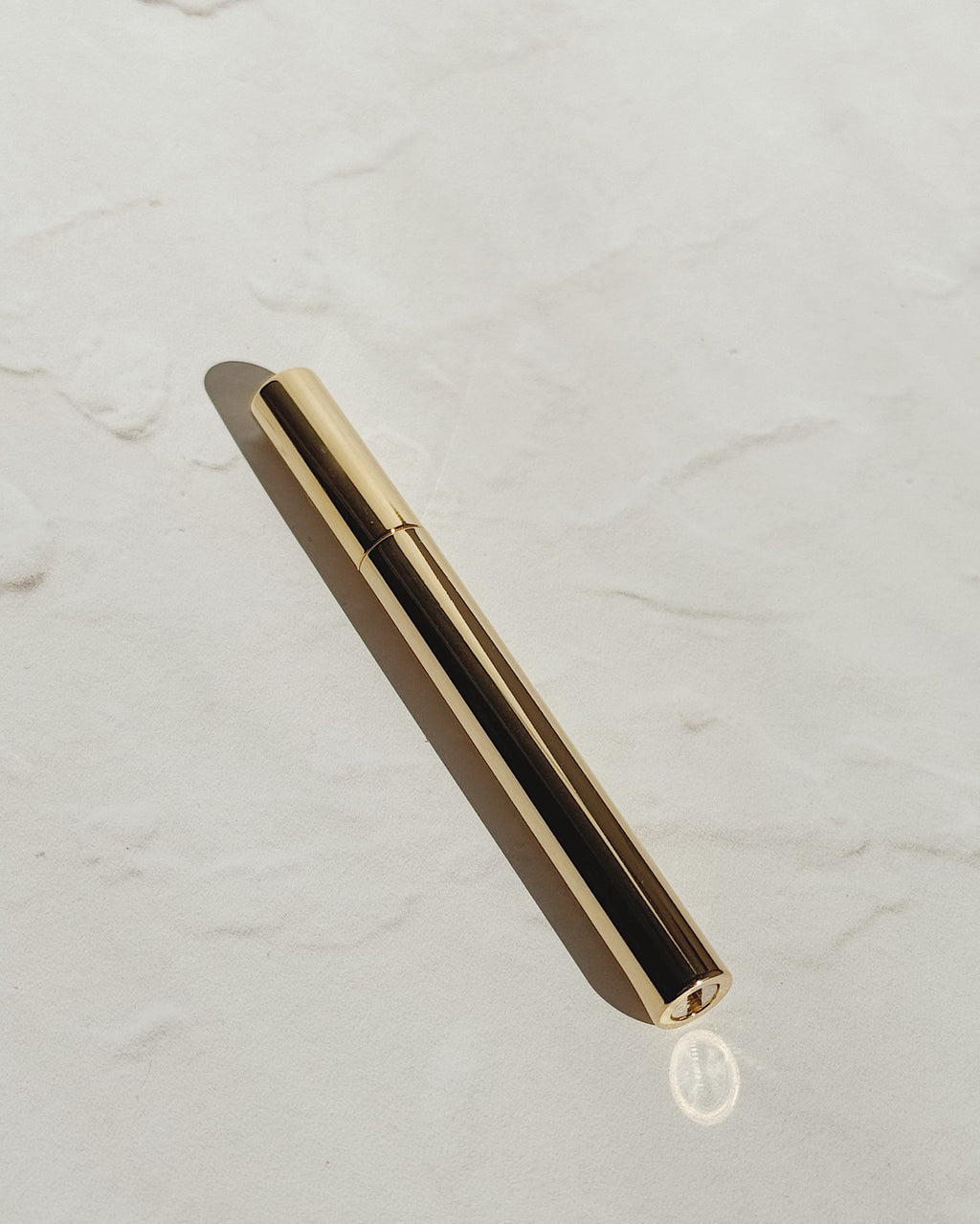 Gold Tsubota Pearl Sigaretta stick lighter with its cap on, resting diagonally on a pale textured surface.