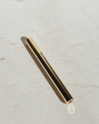 Gold Tsubota Pearl Sigaretta stick lighter with its cap on, resting diagonally on a pale textured surface.