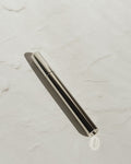 Silver Tsubota Pearl Sigaretta stick lighter with its cap on, resting diagonally on a pale textured surface.