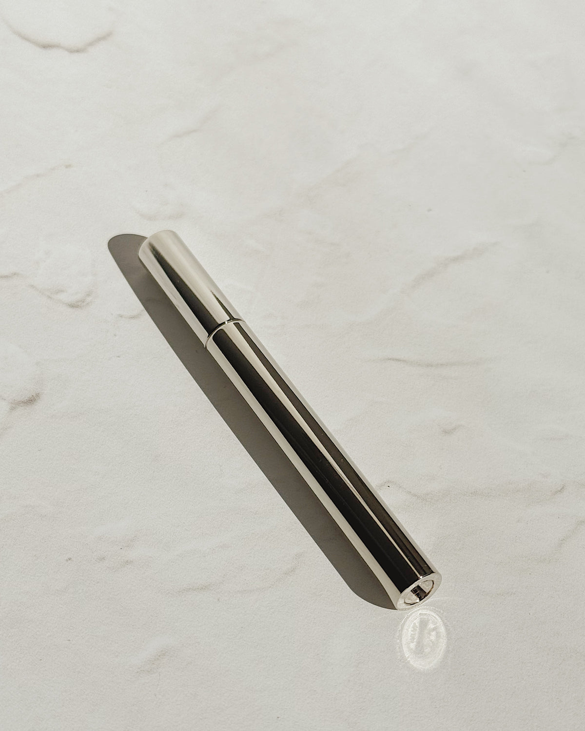Silver Tsubota Pearl Sigaretta stick lighter with its cap on, resting diagonally on a pale textured surface.