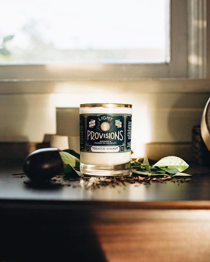 Tobacco Walnut candle on wooden shelf in golden natural light with tobacco pipe and leaves in background