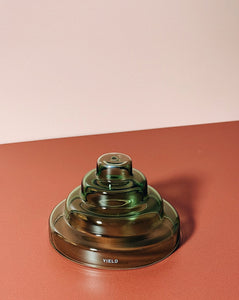 Green glass meso incense holder with 'Yield' branding on a red surface and beige background