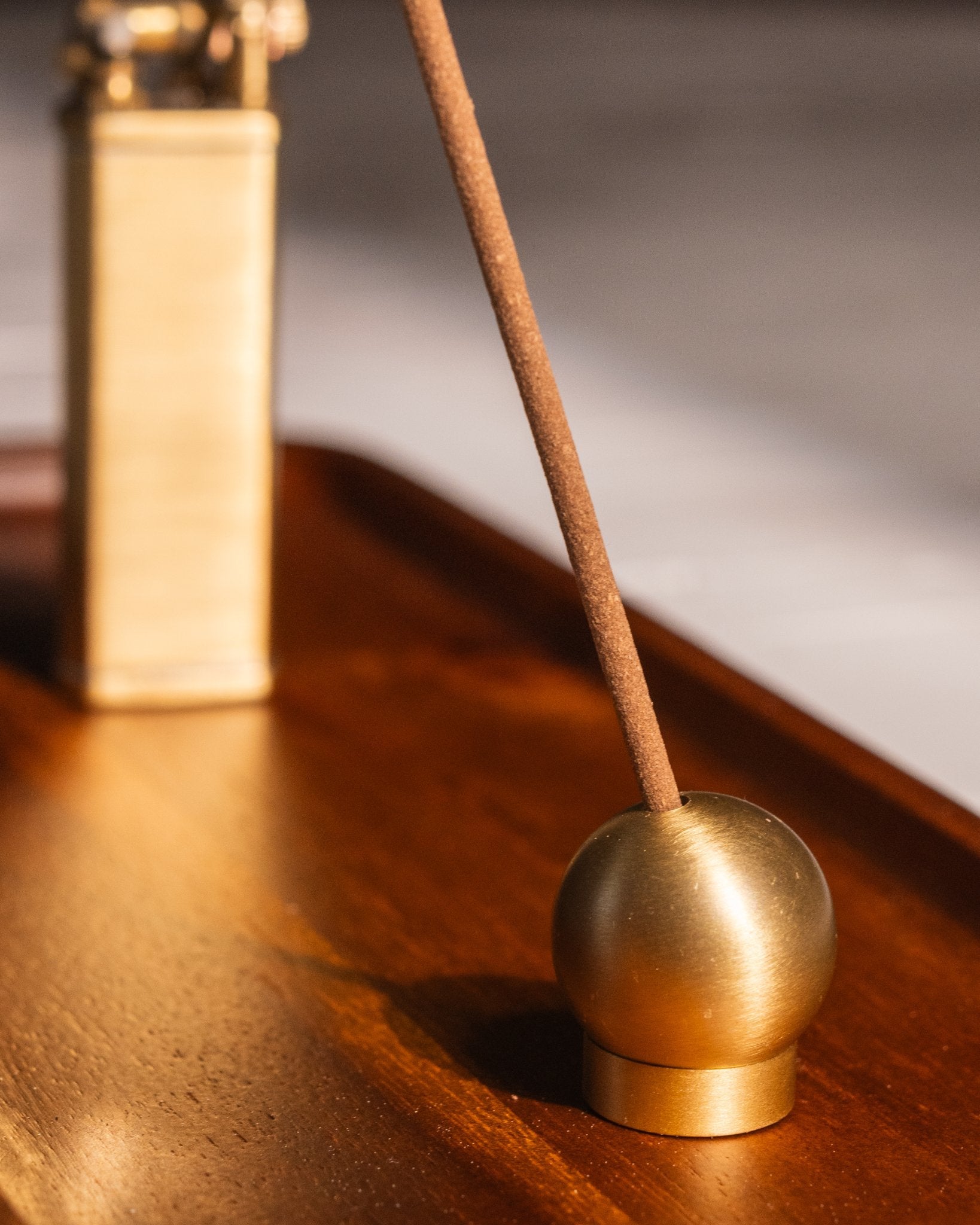 Close-up of sphere brass adjustable incense holder with incense stick, on teakwood tray with bolbo lighter in background
