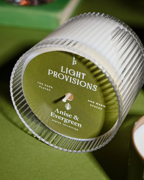 Light Provisions Anise & Evergreen candle tin resting on green surface with ribbed lid and soft shadows