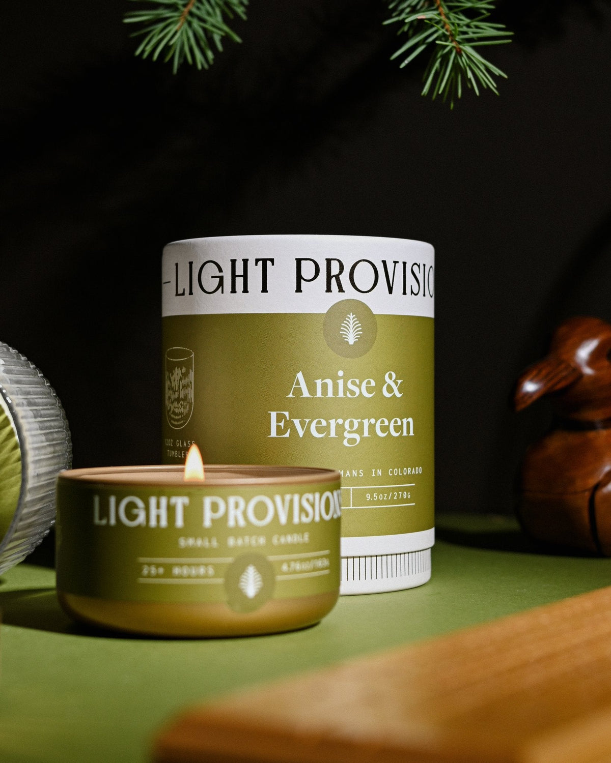 Anise & Evergreen candles and boxes arranged on table with pine branches and wood game board nearby