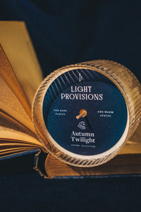 Close-up of Autumn Twilight candle tin lid on an open book with gold-edged pages.