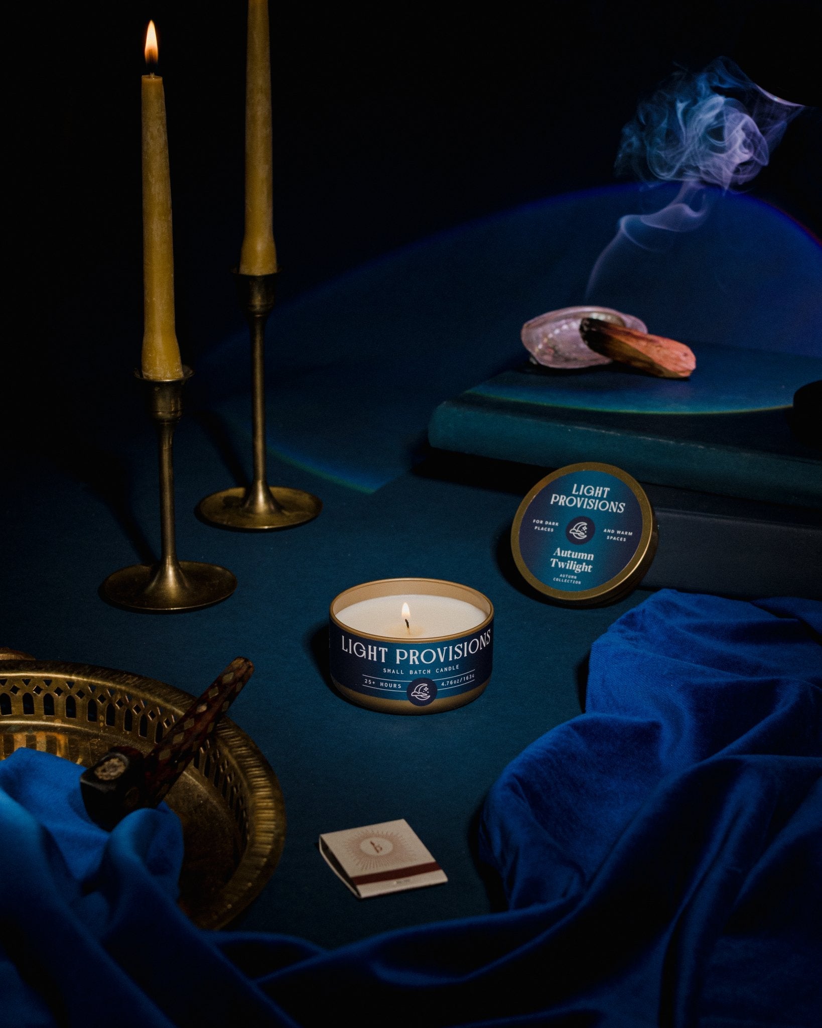 Light Provisions Autumn Twilight candles glass tumbler and travel tin with blue velvet, brass candlesticks, books, and smudge