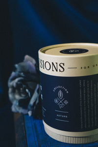 Autumn Twilight glass tumbler candle beside navy and cream packaging tube on dark blue velvet fabric.