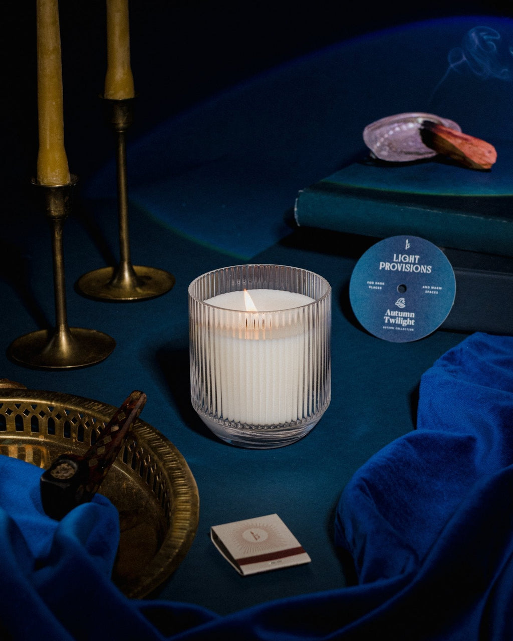 Light Provisions Autumn Twilight candle in glass tumbler with brass candlesticks and deep blue velvet backdrop