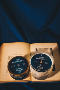 Autumn Twilight candle in signature glassware and matching travel tin resting on an open book.