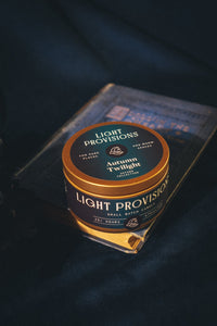 Autumn Twilight travel tin candle on dark blue fabric with warm, moody lighting.