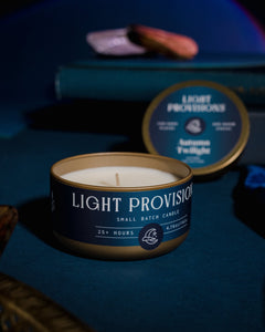 Autumn Twilight candle travel tin open with warm glow on dark blue tabletop with books and velvet