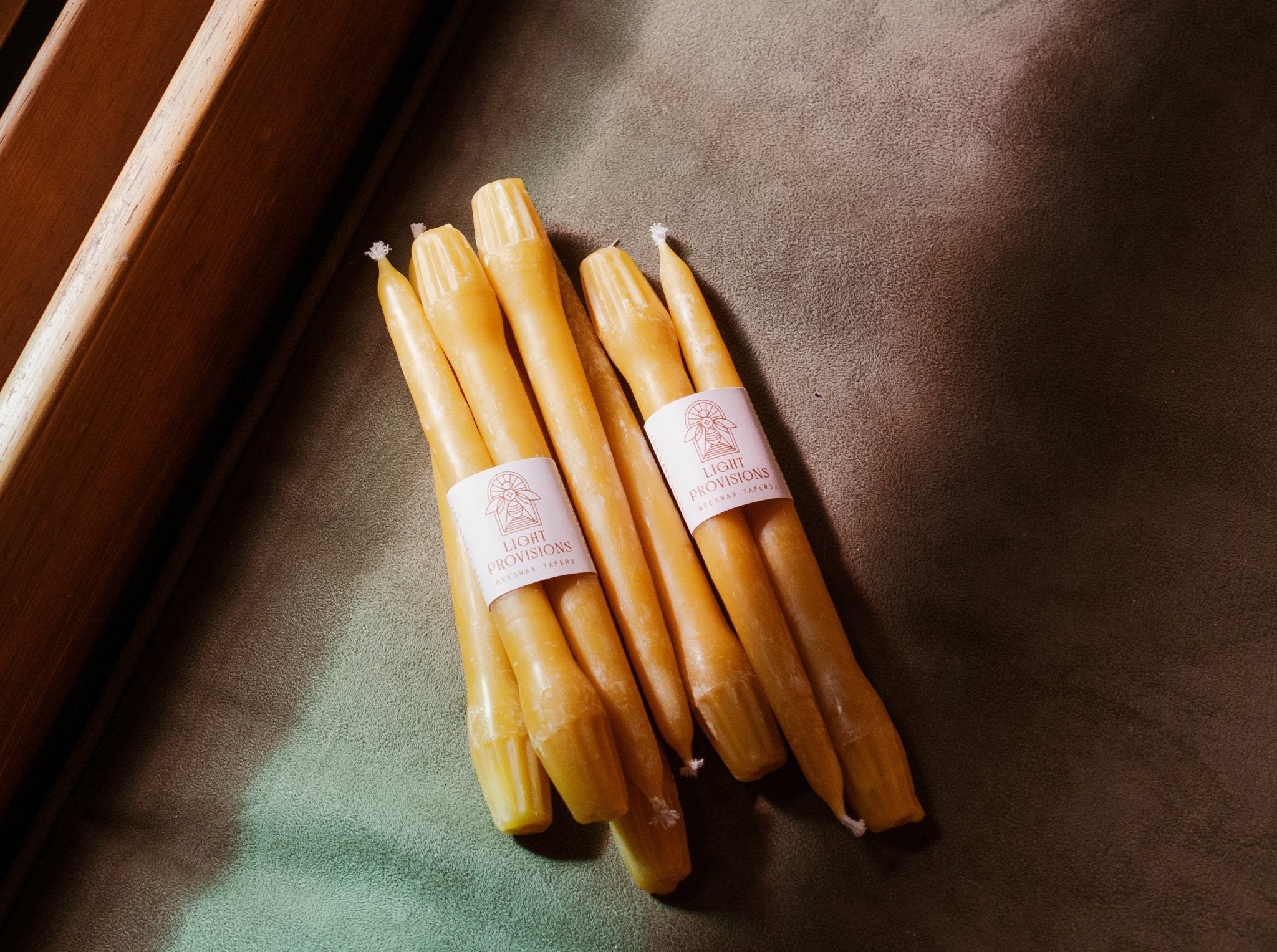 stack of beeswax candles sitting on a church pew with stained glass light in shades of blue and pink