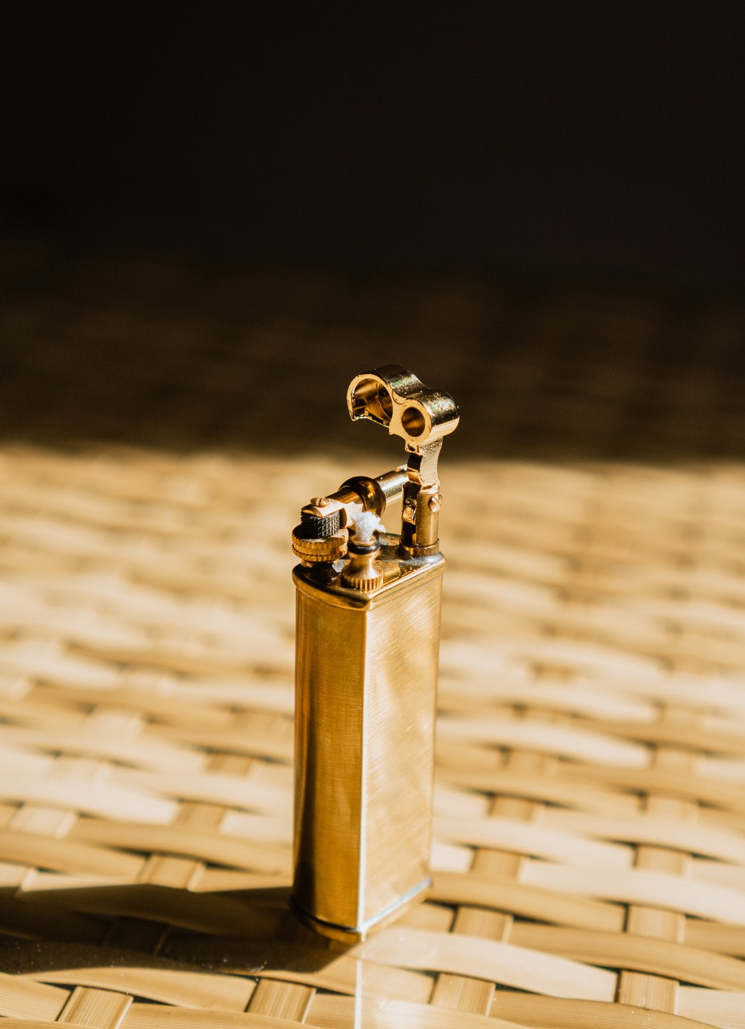 Brass Bolbo Petrol Lighter by Tsubota Pearl standing in warm light on woven bamboo background.