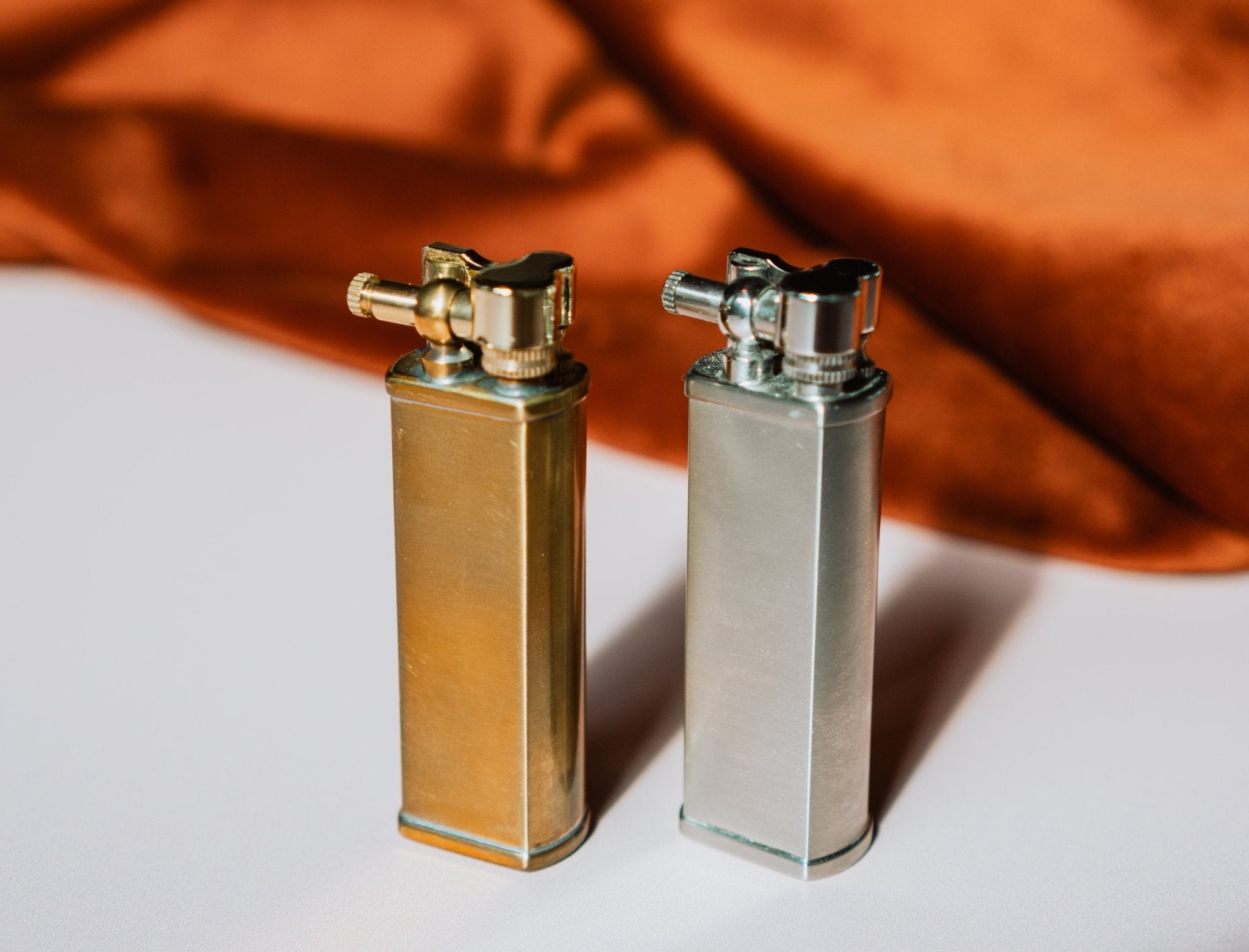 Brass and steel Bolbo Petrol Lighters by Tsubota Pearl on fabric backdrop, refillable Japanese design.