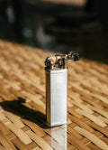 Silver Bolbo Petrol Lighter by Tsubota Pearl in sunlight on woven bamboo, refillable Japanese lighter.