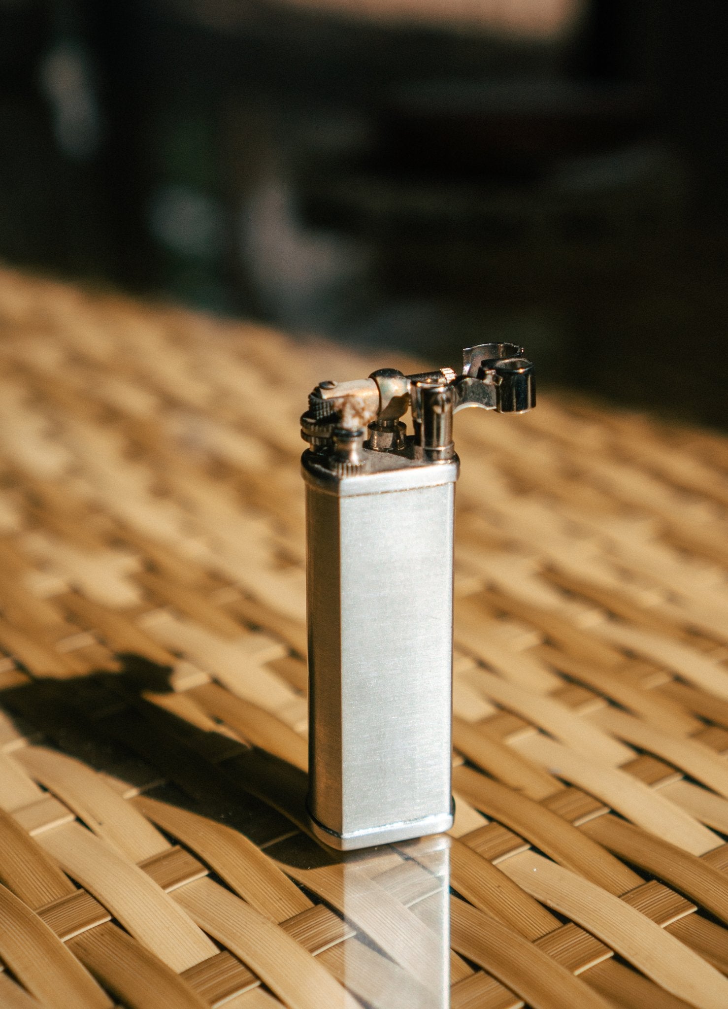 Silver Bolbo Petrol Lighter by Tsubota Pearl in sunlight on woven bamboo, refillable Japanese lighter.