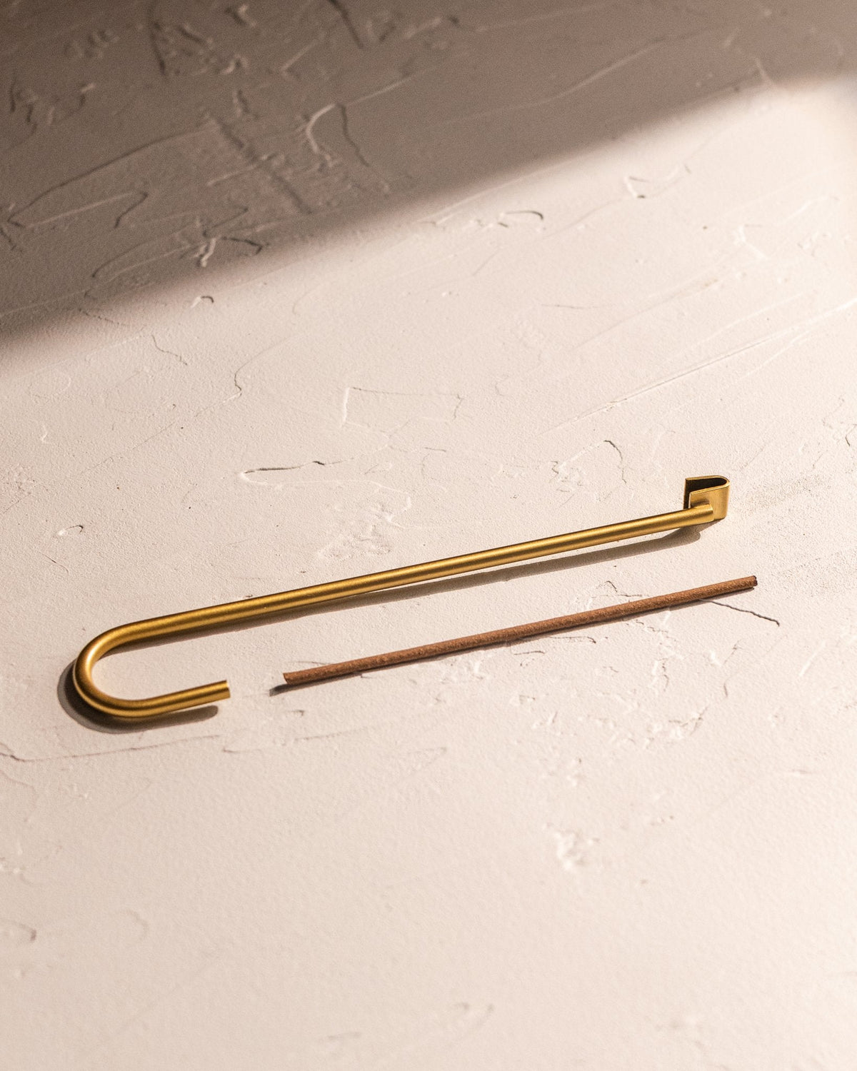 Close-up of curved brass-finished incense holder with incense stick