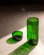 Brass hook incense holder hanging inside green recycled bottle vase with burning incense