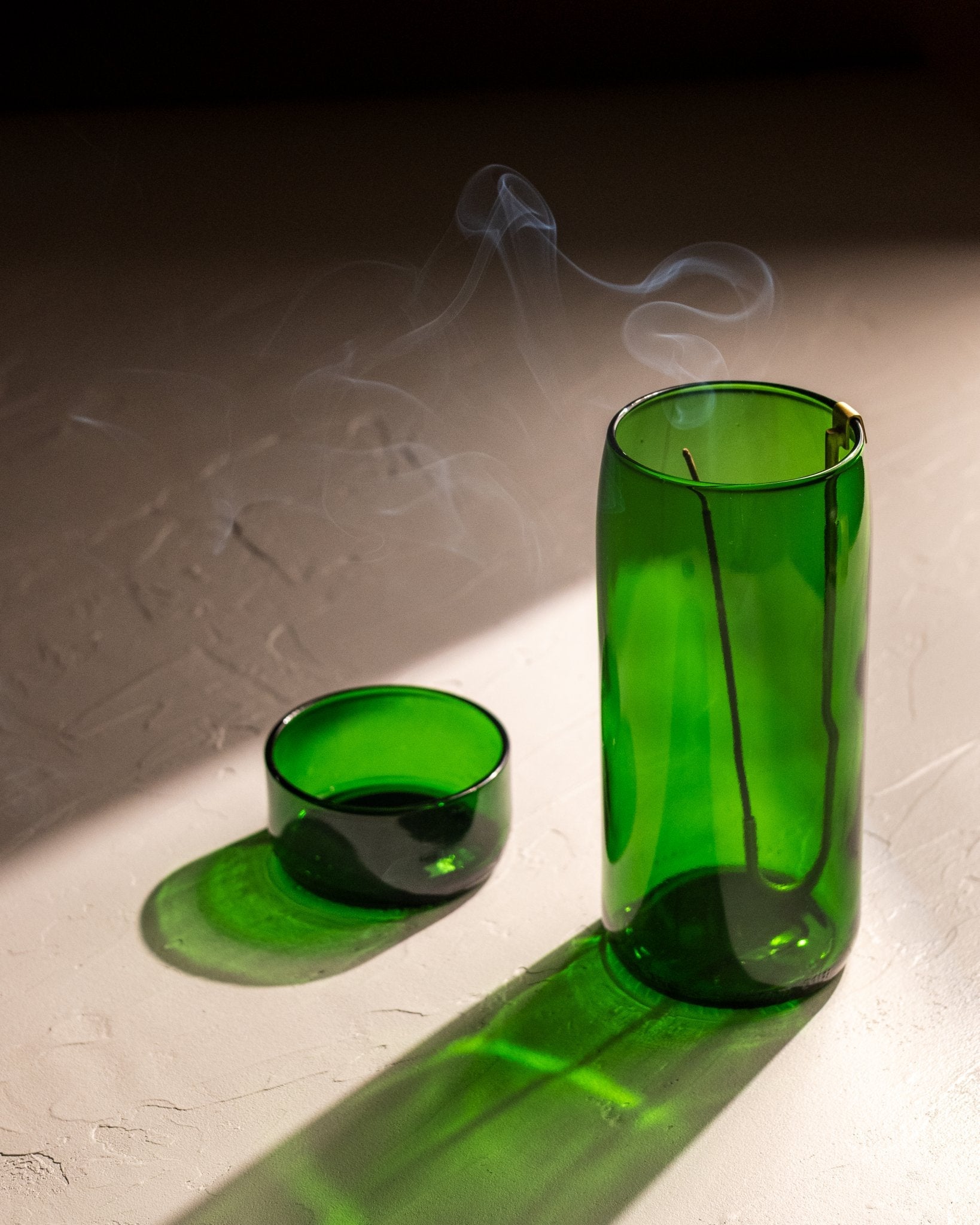 Brass hook incense holder hanging inside green recycled bottle vase with burning incense