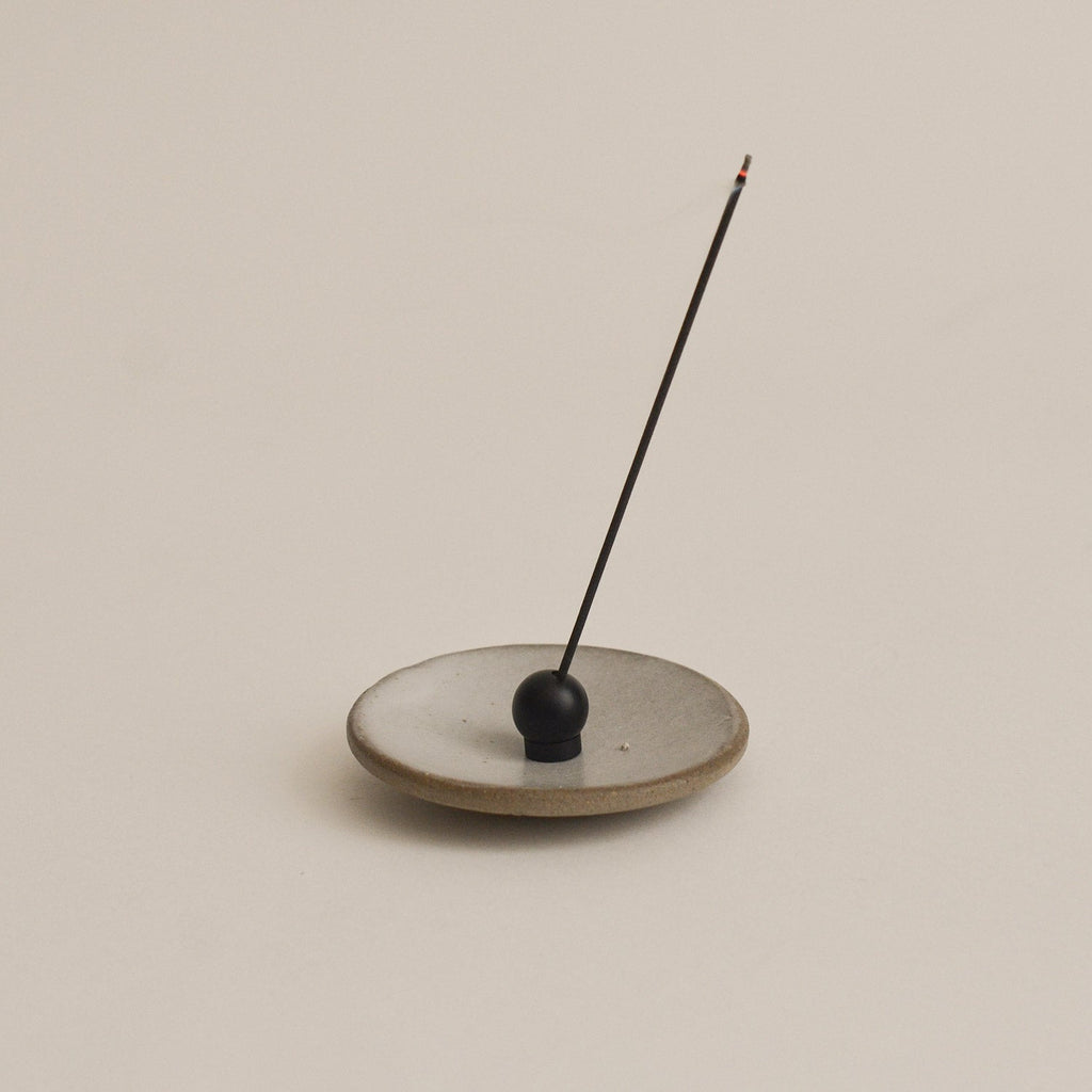 black sphere incense holder with a single incense stick on a beige background