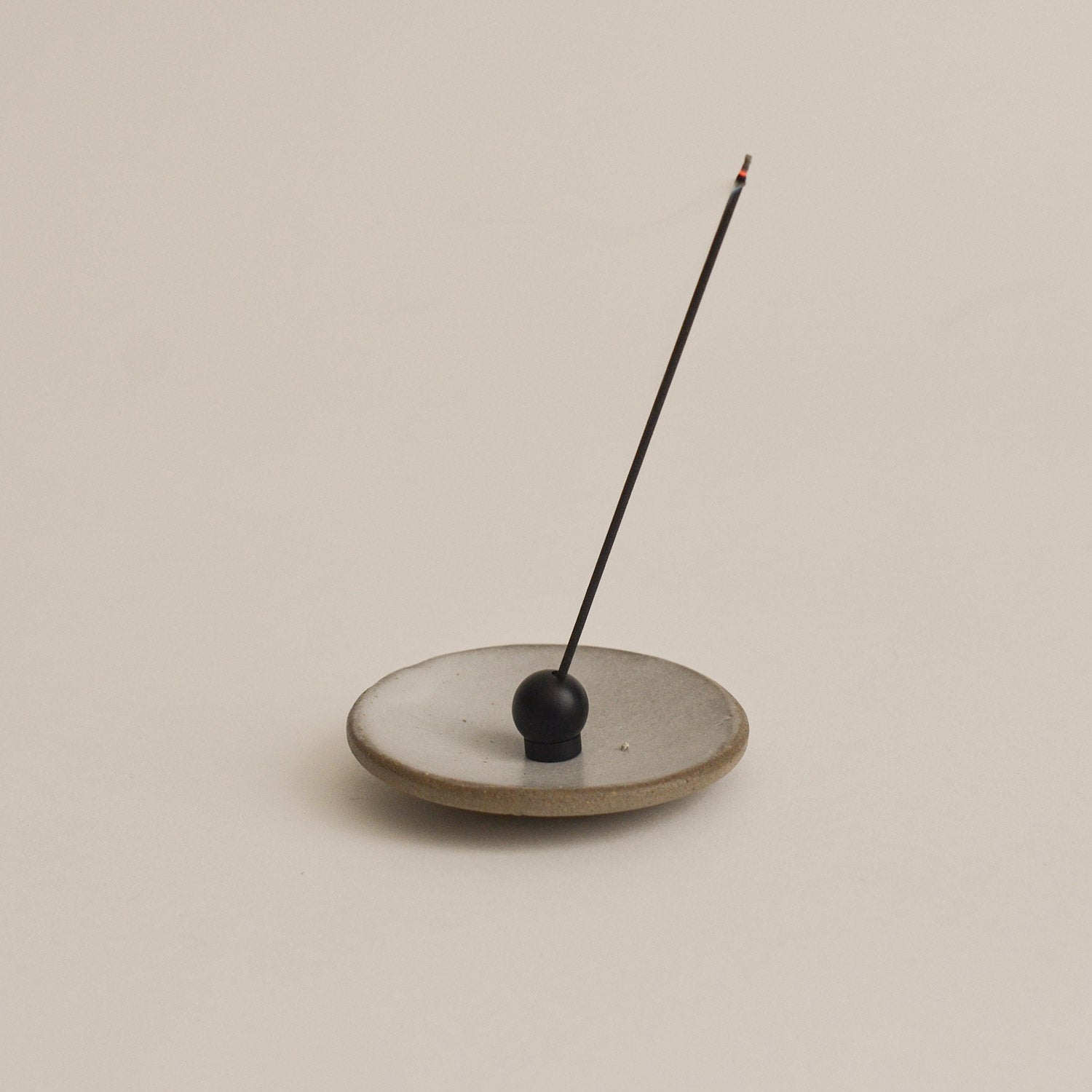 black sphere incense holder with a single incense stick on a beige background