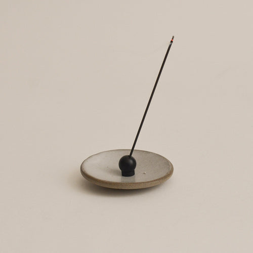 black sphere incense holder with a single incense stick on a beige background