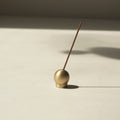 Brass Sphere incense holder with a single incense stick on a beige surface