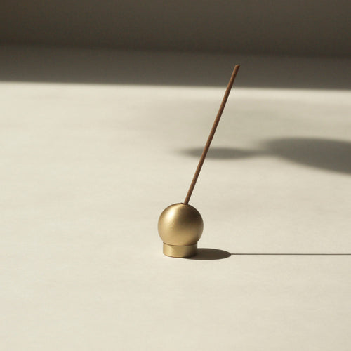 Brass Sphere incense holder with a single incense stick on a beige surface