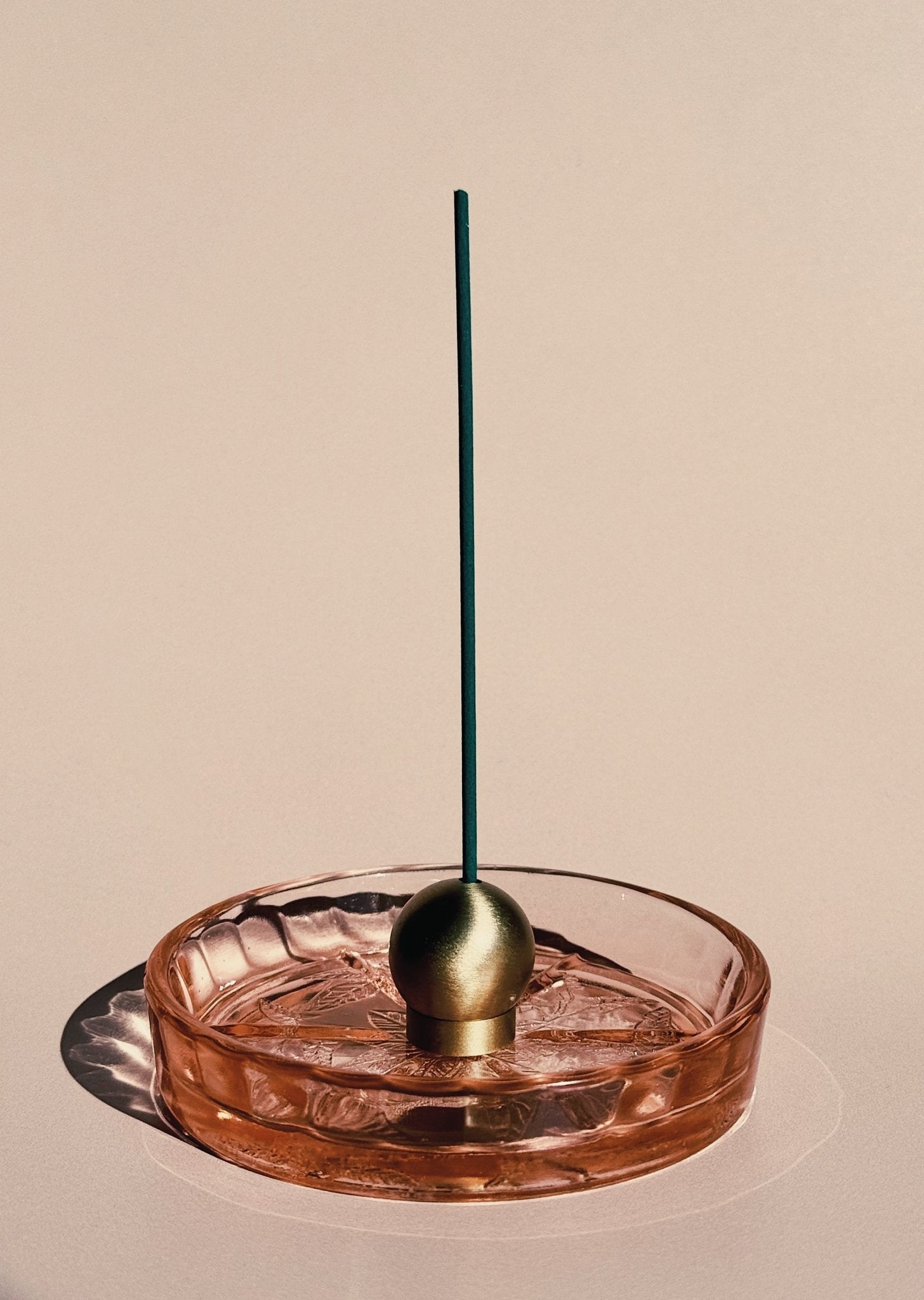 brass sphere incense holder with a green incense stick on a beige background