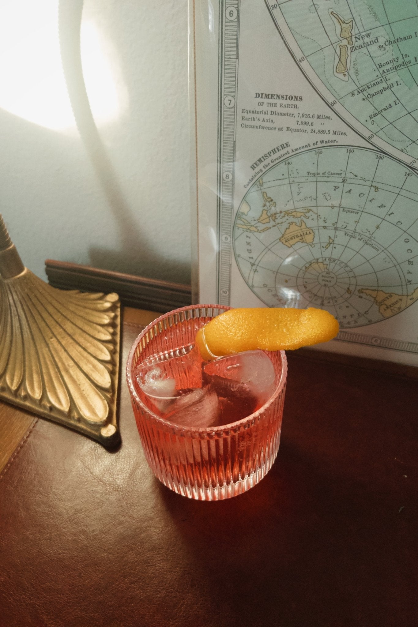 Ribbed glass tumbler holding a negroni cocktail and an orange peel garnish, photographed indoors beside a vintage map