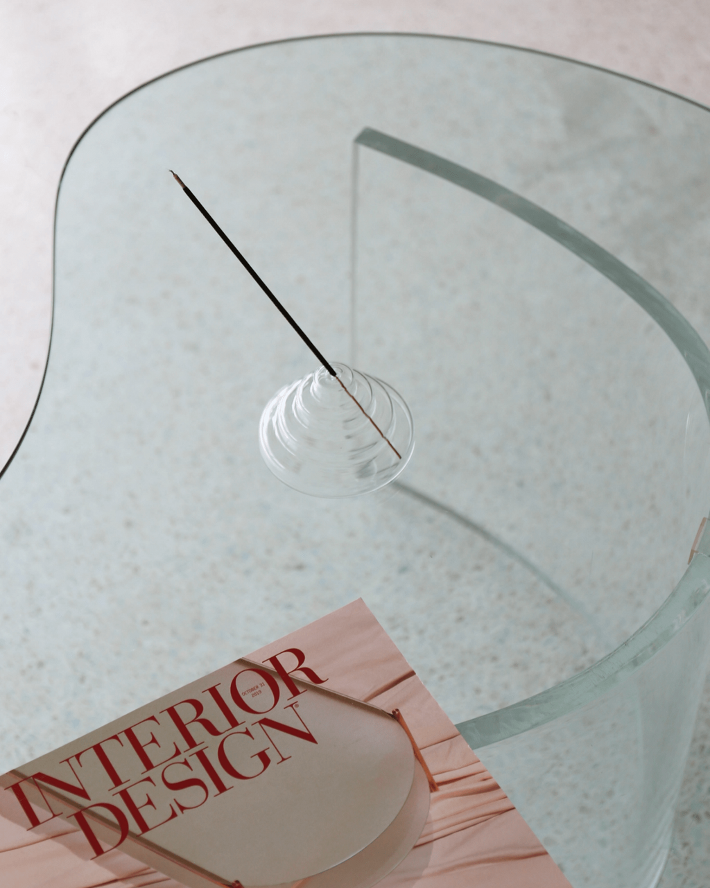 Clear meso incense holder on Glass table with a book titled 'Interior Design' on a light background
