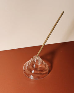 Incense stick in a clear glass stepped holder on a two-tone background