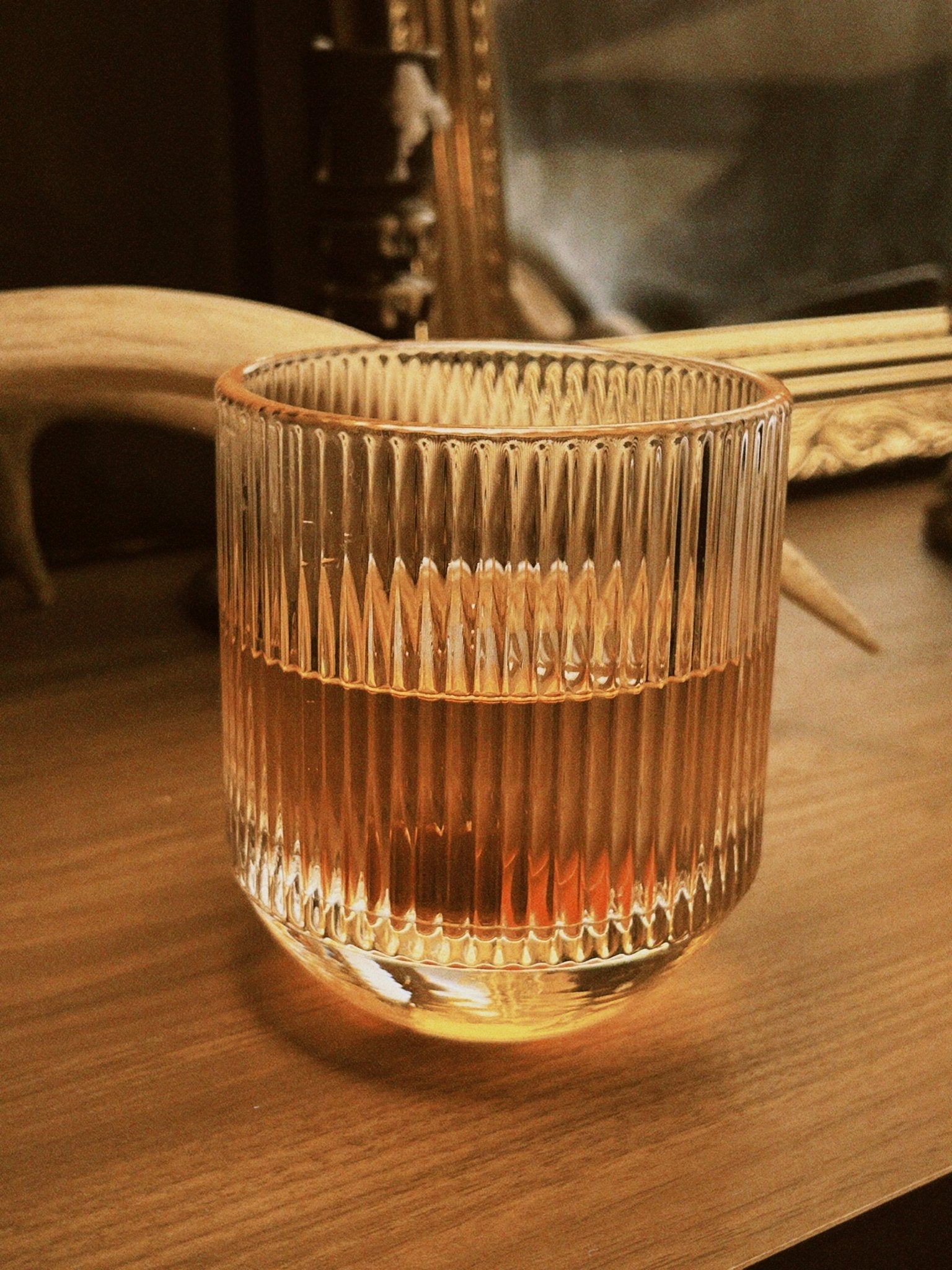 Fluted glass tumbler containing whiskey on a vintage surface