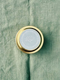 Elderflower & Driftwood 2 oz sample tin seen from a top down view on a green linen surface