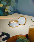 Lit Eucalyptus & Amber candle on table with green sprigs and branded matches  nearby, creating a calm, wintery glow